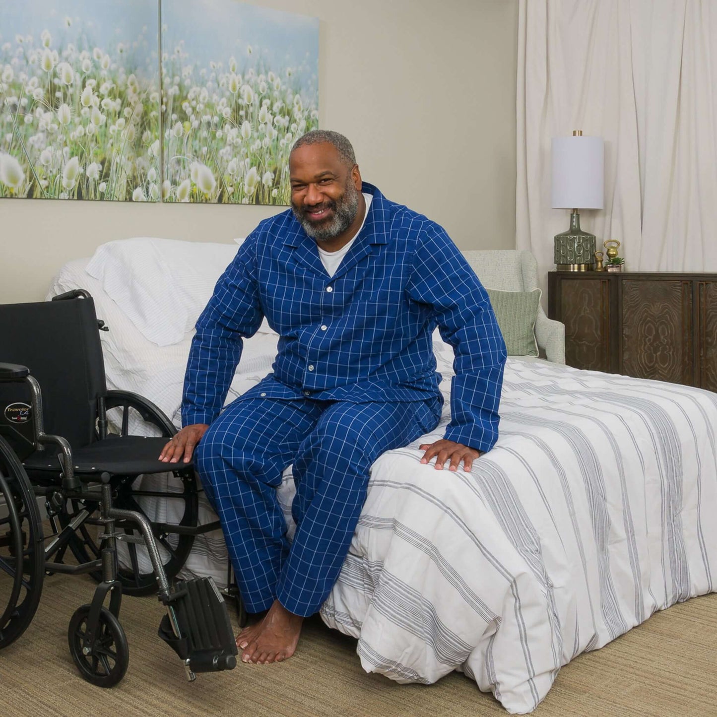 Man in pajamas sitting on bed next to wheelchair, showcasing the Transfer Master Supernal 5 Hi-Low Adjustable Bed.